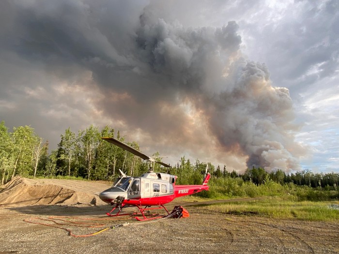 A helicopter sits on the ground with a wildland fire in the background.