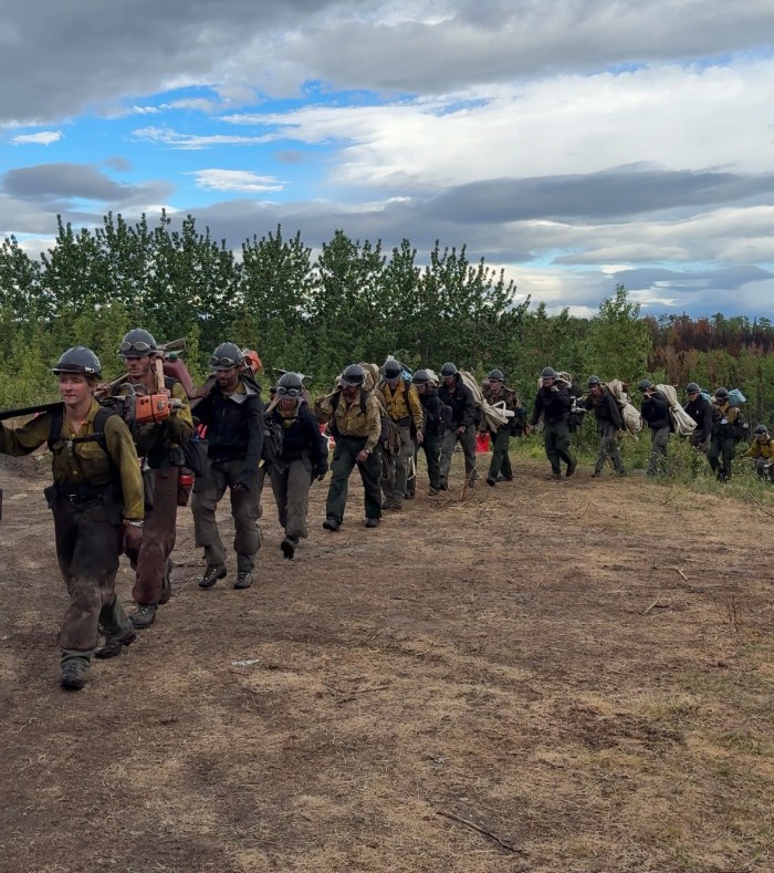 Firefighters carrying gear and equipment, walking back to camp in a line.