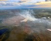 Light-colored smoke rises from the tundra in an aerial photo of a wildfire taken from an air attack plane.