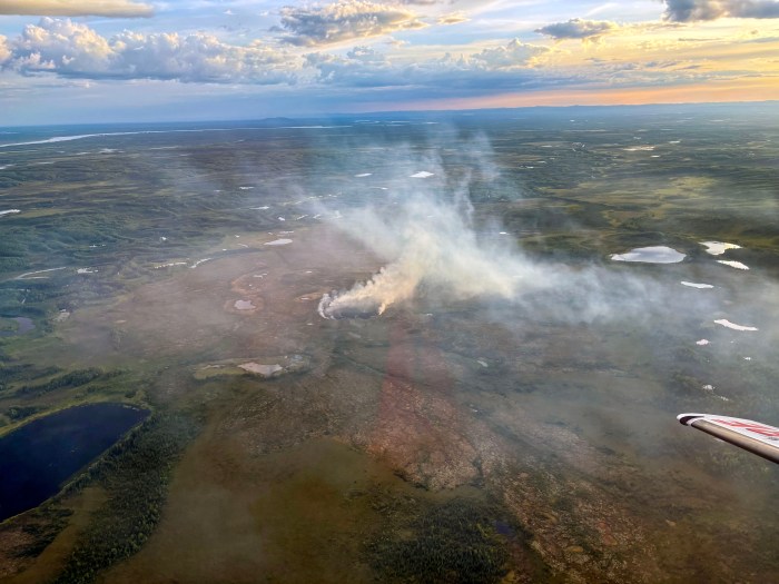 Light-colored smoke rises from the tundra in an aerial photo of a wildfire taken from an air attack plane.