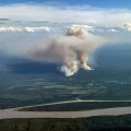 Two columns of wildfire smoke are shown rising from the ground in a photo taken from an airplane. The Yukon River is seen in the foreground.