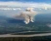 Two columns of wildfire smoke are shown rising from the ground in a photo taken from an airplane. The Yukon River is seen in the foreground.