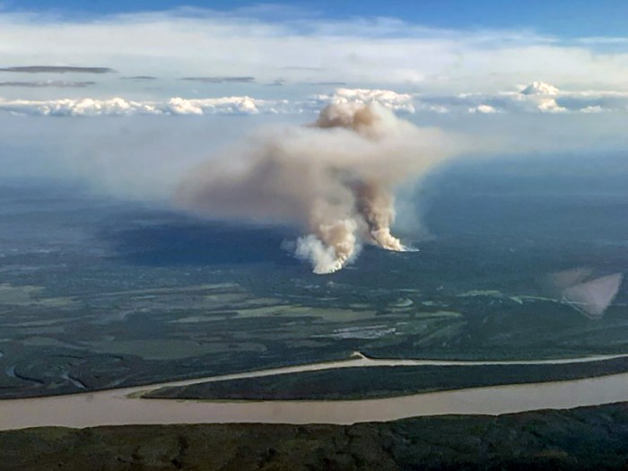 Two columns of wildfire smoke are shown rising from the ground in a photo taken from an airplane. The Yukon River is seen in the foreground.