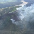 Smoke rising from ridgetop with mosaic of burned and unburned spruce trees. Yukon River in the background and airplane wing tip is at the right edge of the photo.