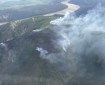 Smoke rising from ridgetop with mosaic of burned and unburned spruce trees. Yukon River in the background and airplane wing tip is at the right edge of the photo.