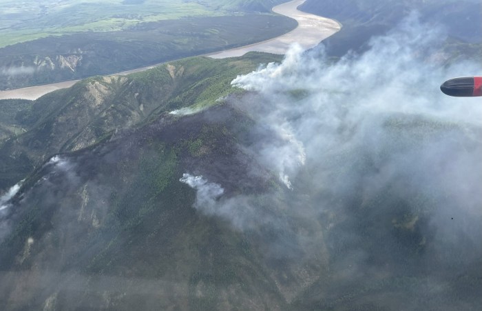 Smoke rising from ridgetop with mosaic of burned and unburned spruce trees. Yukon River in the background and airplane wing tip is at the right edge of the photo.
