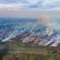 Light-colored wildfire smoke is seen rising from a mostly green landscape in a photo taken from the air.