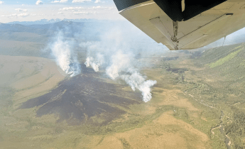 Smoke billows up from a large tundra fire as seen from an airplane.