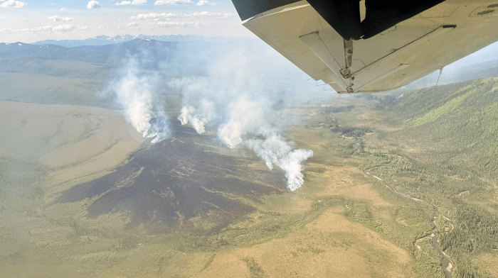 Smoke billows up from a large tundra fire as seen from an airplane.