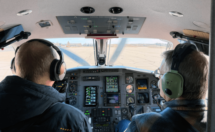 Two men sitting in the cockpit of an airplane waiting to take off at an air strip.