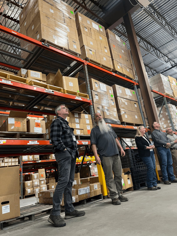 Five people standing in front of cardboard boxes stacked on large shelves in a large warehouse.