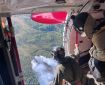 Two people look out from an open airplane door at smoke rising up from a forest fire below.