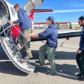 Three men board a red and white plane.