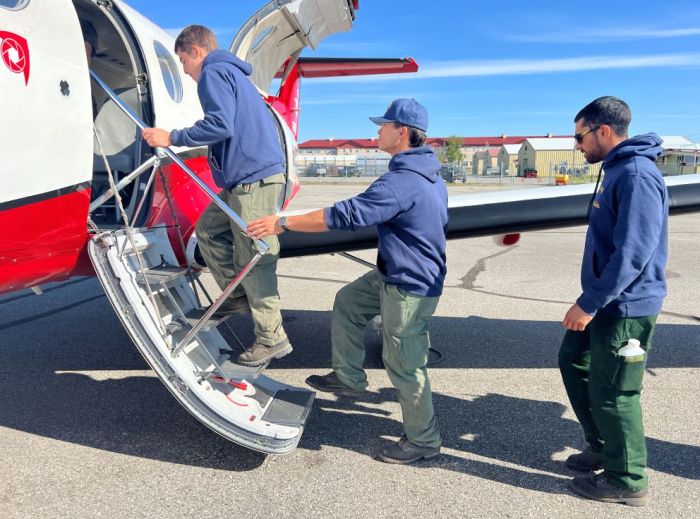 Three men board a red and white plane.