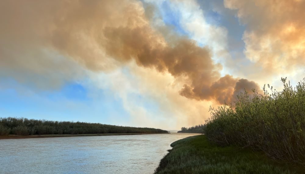 A large column of smoke drifts up from a forest fire burning next to a driver