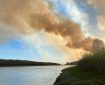 A large column of smoke drifts up from a forest fire burning next to a driver