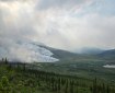Smoke rises from the low-intensity Nutmeg Fire in a broad tundra valley surrounded by low mountains under a cloudy sky.