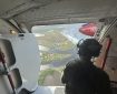 A person sitting in the doorway of an airplane looks at smoke billowing up for a fire near a town
