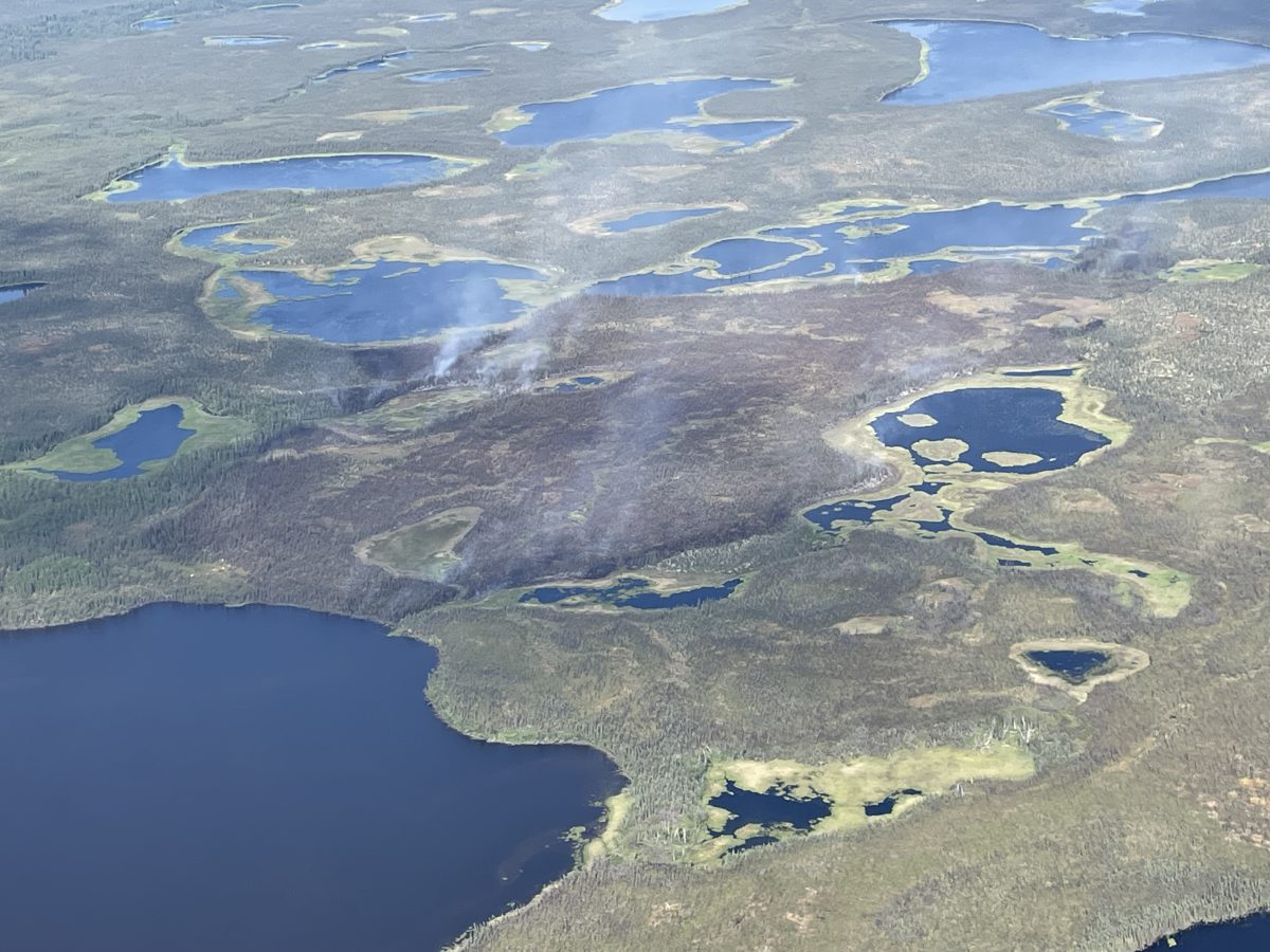 Photo of a blackened burned area between lakes showing small wisps of smoke.