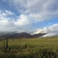 Smoke billows from a low-intensity fire in the mountains with a green tundra foreground.