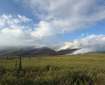 Smoke billows from a low-intensity fire in the mountains with a green tundra foreground.