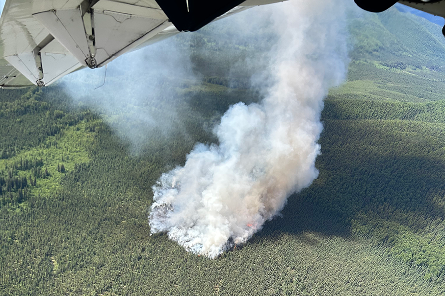 Smoke billows up from a forest fire as seen from an airplane flying overhead.