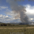 A large smoke column rises up from the ground in the distance.