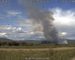 A large smoke column rises up from the ground in the distance.