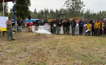 IC Jake Livingston stands in front of a map to the left, while firefighters are gathered listening to the right.