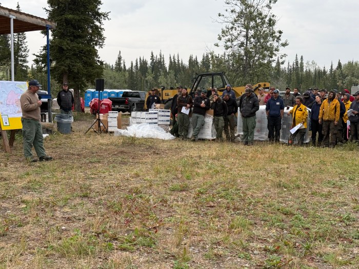 IC Jake Livingston stands in front of a map to the left, while firefighters are gathered listening to the right.