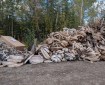 A large pile of used fire hose and metal fittings sits on a gravel lot at the edge of a wooded area, awaiting cleaning, inspection, and repacking after wildfire operations.
