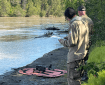Two firefighters stand on a river bank looking at a drone sitting on an orange fabric platform.
