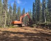 An orange tracked excavator works on a cleared fire line in a boreal forest, moving soil and woody debris during suppression-repair operations on the Mukluk Fire.