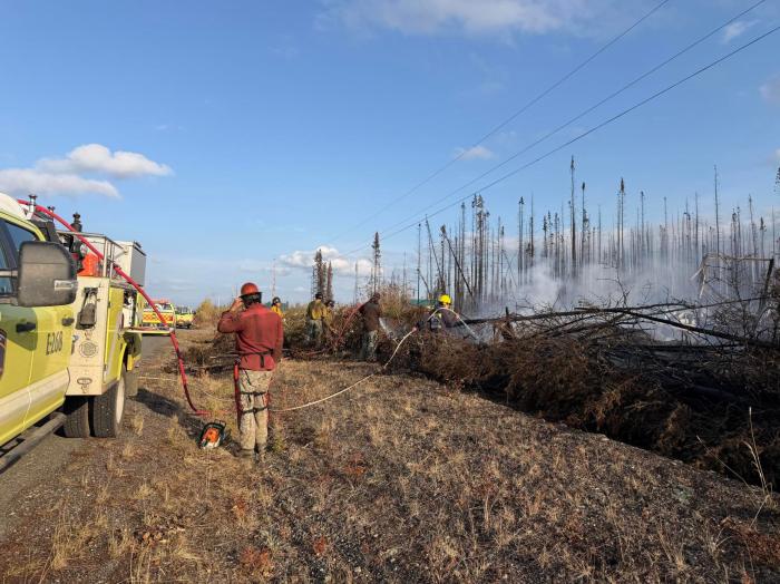 Firefighters and engines respond to smoke and burning vegetation near Red Fox Drive, with power lines overhead.