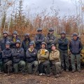 Members of the TCC crew gather in two rows in a forested area affected by the Mukluk Fire.