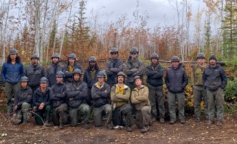 Members of the TCC crew gather in two rows in a forested area affected by the Mukluk Fire.