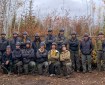 Members of the TCC crew gather in two rows in a forested area affected by the Mukluk Fire.