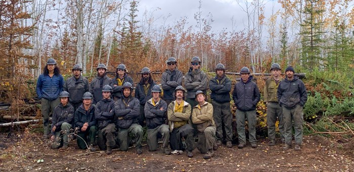 Members of the TCC crew gather in two rows in a forested area affected by the Mukluk Fire.